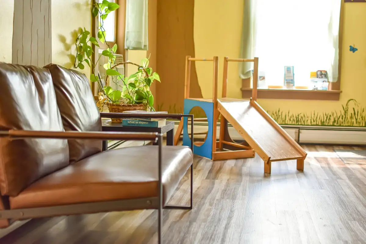 The waiting area at South Royalton Health Center, with a wooden climbing slide, armchairs and houseplants by the window.